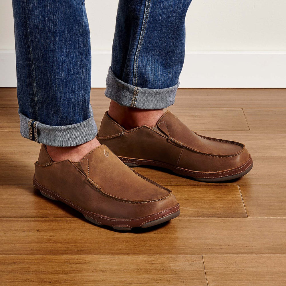 Olukai Moloa. Men's slip-on shoe in brown waxed nubuck leather. Model wearing jeans.