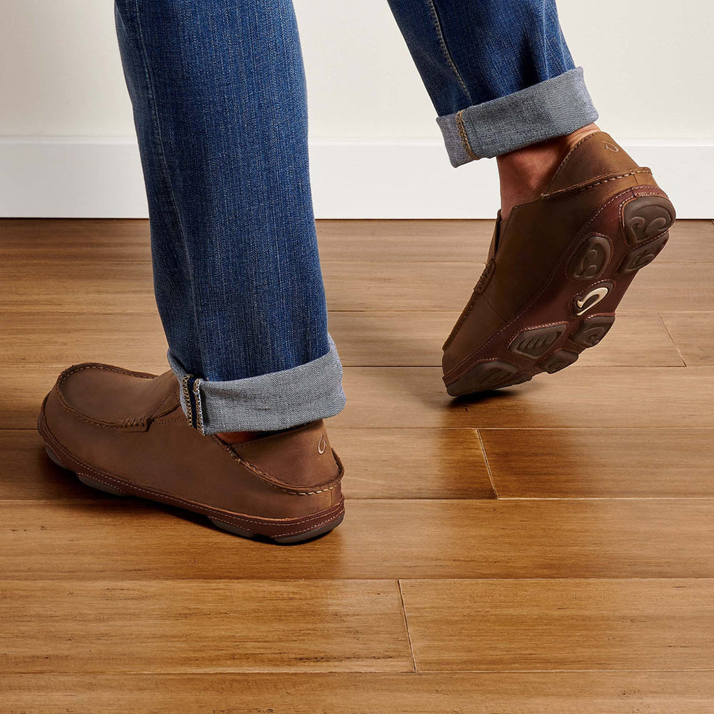 Olukai Moloa. Men's slip-on shoe in brown waxed nubuck leather. Model wearing shoes, back view.