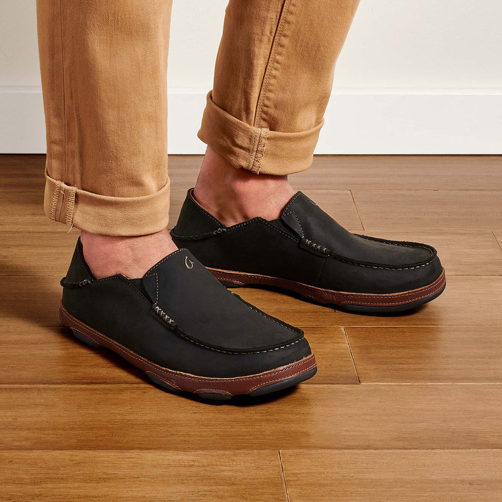 Olukai Moloa. Men's slip-on shoe in black waxed nubuck leather. Model wearing khaki pants.